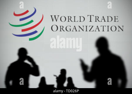 Die World Trade Organisation Logo ist auf einen LED-Bildschirm in der Silhouette gesehen, während eine Person ein Smartphone verwendet im Vordergrund (nur redaktionelle Nutzung) Stockfoto