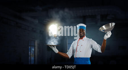 Schwarzer Mann das Tragen einer Schürze und Kochen in Aktion. Mixed Media Stockfoto