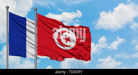 Frankreich und Tunesien Flagge im Wind gegen Weiße bewölkt blauer Himmel zusammen. Diplomatie Konzept, internationale Beziehungen. Stockfoto