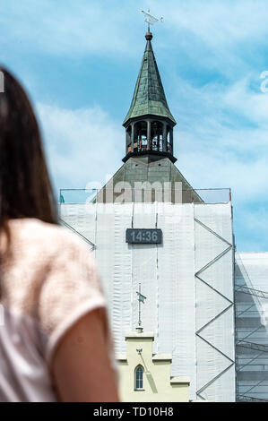 Deggendorf, Deutschland. 11 Juni, 2019. Eine Frau schaut sich eine digitale Zeitanzeige auf dem Rathausturm. Da das Alte Rathaus eingeschlossen war, die Uhr der Turm hat auch versteckt. Bis voraussichtlich Mitte Juli, zwei LED-Panels über dem Gerüst wird die Zeit angezeigt. Foto: Armin Weigel/dpa/Alamy leben Nachrichten Stockfoto