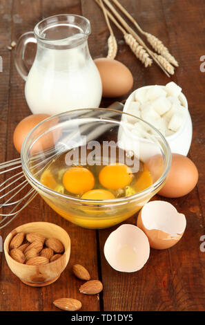 Gebrochene Eier in der Schale und verschiedene Zutaten neben sie auf Holztisch close-up Stockfoto