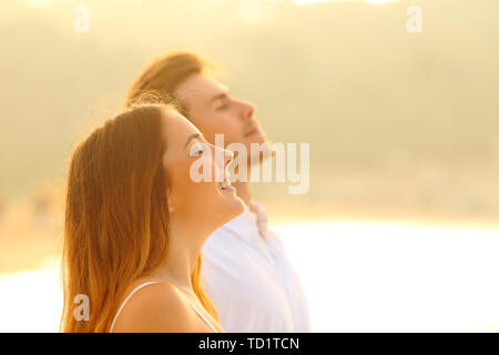 Seitenansicht Portrait von ein glückliches Paar am Strand, atmen tief die frische Luft bei Sonnenuntergang Stockfoto
