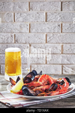 Eine Mischung aus Muscheln, Muscheln und Garnelen mit einem Glas aufgeschäumte Bier und eine Mauer im Hintergrund, vertikale Ansicht von oben Stockfoto