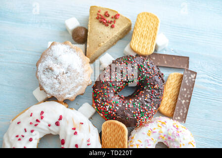 Schädliche süße Nahrungsmittel auf Blau Holz- Hintergrund. Donuts, Muffins, Schokolade auf dem Tisch stapeln. Das Konzept der ungesunde Ernährung und Übergewicht. Der Blick f Stockfoto