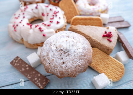 Schädliche süße Nahrungsmittel auf Blau Holz- Hintergrund. Donuts, Muffins, Schokolade auf dem Tisch stapeln. Das Konzept der ungesunde Ernährung und Übergewicht. Der Blick f Stockfoto