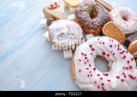 Schädliche süße Nahrungsmittel auf Blau Holz- Hintergrund. Donuts, Muffins, Schokolade auf dem Tisch stapeln. Das Konzept der ungesunde Ernährung und Übergewicht. Der Blick f Stockfoto