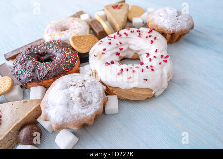 Schädliche süße Nahrungsmittel auf Blau Holz- Hintergrund. Donuts, Muffins, Schokolade auf dem Tisch stapeln. Das Konzept der ungesunde Ernährung und Übergewicht. Der Blick f Stockfoto