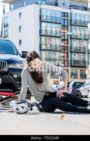 Die volle Länge eines Verletzten jungen Frau, bei denen schwere Schmerzen durch Knie-verstauchung oder Bruch verursacht nach Fahrradunfall in der Stadt Stockfoto