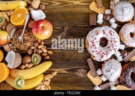 Ungesunde und gesunde Süßigkeiten auf Holz- Hintergrund. Biologische und diätetische Lebensmittel und das Problem der Verweigerung von schädlichen Desserts. Früchte und Nüsse vs Donut Stockfoto