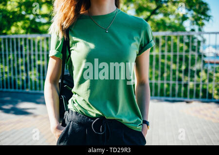 Stilvolle junge Frau stehend an sonnigen, grünen Straße. Weibliche tragende t-shirt ihre Hände in den Taschen. Close-up Details basic Damen Sommer clot Stockfoto