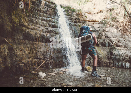 Alleinreisender Mann stand in der Nähe von Great Falls Shulamit fallen in einem flachen Teich mit smaragdgrünem Wasser. Ein Gedi - Naturpark und Nationalpark Stockfoto