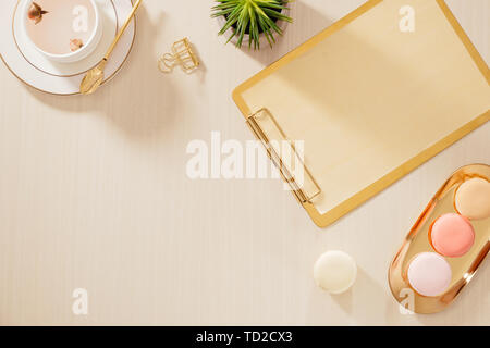 Moderne gold stilisierte home office Schreibtisch mit Ordner-, Makronen, Kaffeetasse auf beigem Hintergrund. Flach, Ansicht von oben lifestyle Konzept." Stockfoto