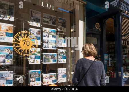 Eine Frau auf der Suche nach Details im Fenster der Immobilienmakler, Dinard, Bretagne, Frankreich Stockfoto