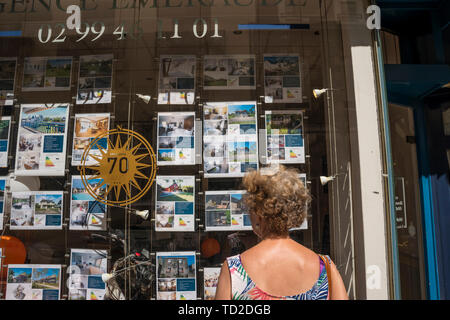 Eine Frau auf der Suche nach Details im Fenster der Immobilienmakler, Dinard, Bretagne, Frankreich Stockfoto