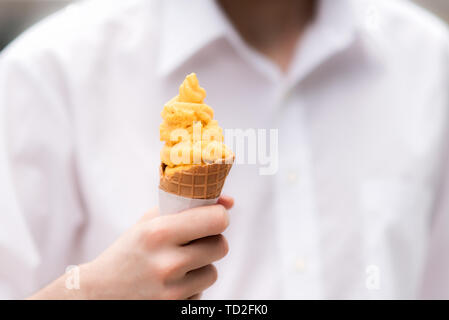 Junger Mann ein weißes Hemd hält ein köstliches Mangosorbet Kegel Stockfoto