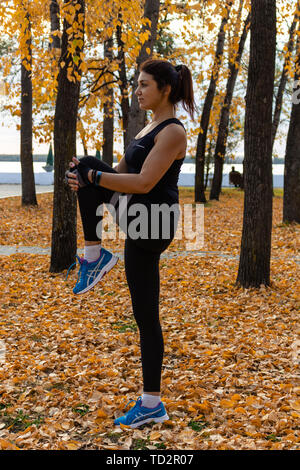 Attraktive Frau im Sport Kleidung Sport übungen in der Natur, auf dem Teppich der Blätter im Herbst, liebt, Gymnastik, Knetet seine Beine. Aktive junge g Stockfoto