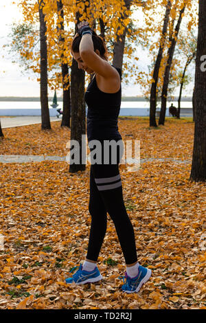 Attraktive Frau im Sport Kleidung Sport übungen in der Natur, auf dem Teppich der Blätter im Herbst, liebt, Gymnastik, Knetet seine Beine. Aktive junge g Stockfoto