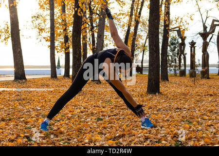 Chabarowsk, Russland - 07.Oktober 2018: Eine attraktive Frau im Sport Kleidung Sport übungen in der Natur gegen den Sonnenuntergang und den Amur, liebt Stockfoto