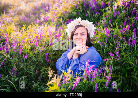 Hübsche Frau mit Blume Kranz in lila Feld. Portrait von Mädchen in Blau Stockfoto