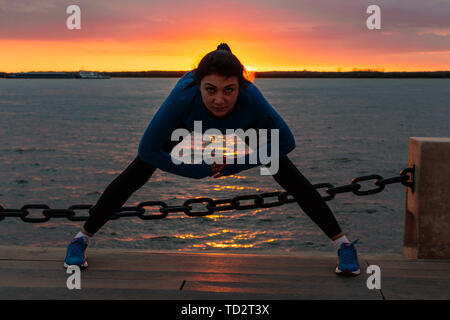 Chabarowsk, Russland - 07.Oktober 2018: Eine attraktive Frau im Sport Kleidung Sport übungen in der Natur gegen den Sonnenuntergang und den Amur, liebt Stockfoto