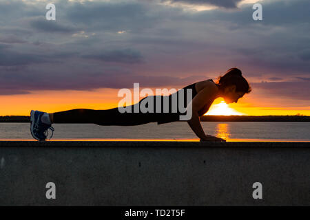 Chabarowsk, Russland - 07.Oktober 2018: Eine attraktive Frau im Sport Kleidung Sport übungen in der Natur gegen den Sonnenuntergang und den Amur, liebt Stockfoto