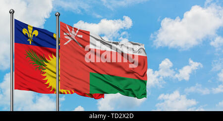 Guadeloupe und Oman Flagge im Wind gegen Weiße bewölkt blauer Himmel zusammen. Diplomatie Konzept, internationale Beziehungen. Stockfoto