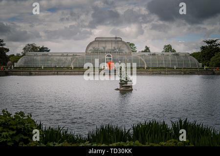 Der Blick auf das Palm House aus über dem Wasser bei Kew Gardens mit geblasenem Glas Skulptur Sommer Sonne, die von Dale Chihuly davor. Stockfoto