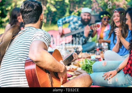 Junge Leute, Picknick und Gitarre spielen im Park - Gruppe der glücklichen Freunde Spaß haben während des Wochenendes im Freien Stockfoto