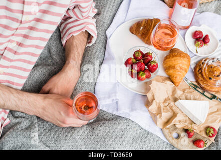Des Menschen Hand Glas Rose Wein, Sommer Picknick mit Käse und Wein auf der Wiese im Stadtpark close-up Stockfoto