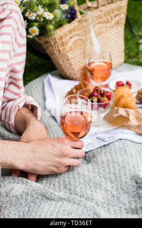 Des Menschen Hand Glas Rose Wein, Sommer Picknick mit Käse und Wein auf der Wiese im Stadtpark close-up Stockfoto