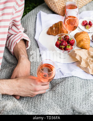 Des Menschen Hand Glas Rose Wein, Sommer Picknick mit Käse und Wein auf der Wiese im Stadtpark close-up Stockfoto