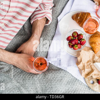 Des Menschen Hand Glas Rose Wein, Sommer Picknick mit Käse und Wein auf der Wiese im Stadtpark close-up Stockfoto
