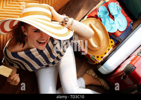 Obere Ansicht von Happy Elegant Frau in weißen Hosen und gestreifte Bluse mit grosse Sommer hat in der Nähe von offenen Reisekoffer Eis essen Verpackung für den Sommer Stockfoto