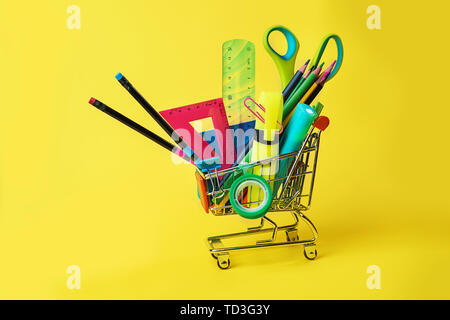Zurück Konzept mit Warenkorb und Bunte Bleistifte zur Schule, Quadrat Lineal, Schere, Clips, Markierungen auf Pastellgelb Kulisse. Stockfoto
