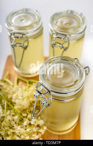 Saft aus den Blüten von einem schwarzen Holunder auf einem weißen Tisch. Therapeutische kalten Sirup vorbereitet für die Lagerung für den Winter. Hellen Hintergrund. Stockfoto