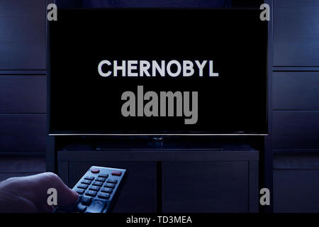 Ein Mann Punkte eine TV-Fernbedienung auf den Fernseher, die Zeigt die Tschernobyl Haupttitel Bildschirm (nur redaktionelle Nutzung).