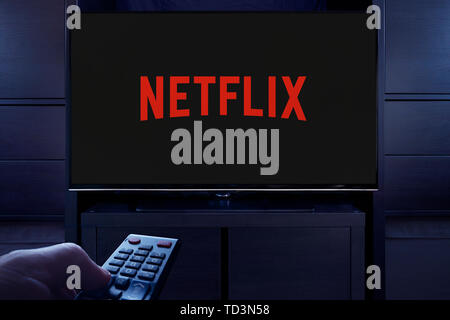 Ein Mann Punkte eine TV-Fernbedienung auf den Fernseher, die zeigt das Logo für die Netflix on demand Video Streaming Service (nur redaktionelle Nutzung). Stockfoto