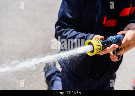 Hände von Feuerwehrmann, kein Gesicht, ein Schlauch durch das Werfen von Wasser unter hohem Druck. Stockfoto