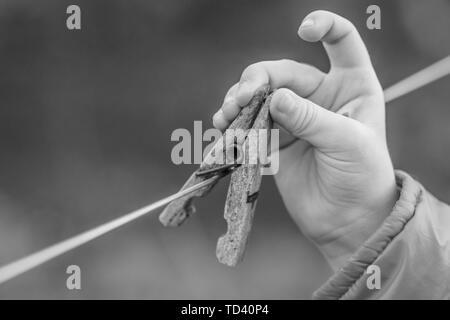 Kinder- Hand berührt die alten hölzernen clothespin auf dem Seile hängt. Close-up, selektive konzentrieren. Schwarz und Weiß Foto Stockfoto