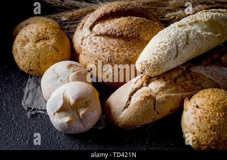 Sortiment von verschiedenen Arten von Brot, Brot, Baguette, Brote, Brötchen mit Ohren von Weizen auf schwarzem Hintergrund, gesunde Konzept, Kopieren spase, Bäckerei pro Stockfoto