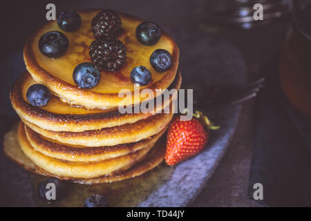 Frische Pfannkuchen mit Ahornsirup und Beeren auf dunklem Hintergrund klassische amerikanische Frühstück Stockfoto