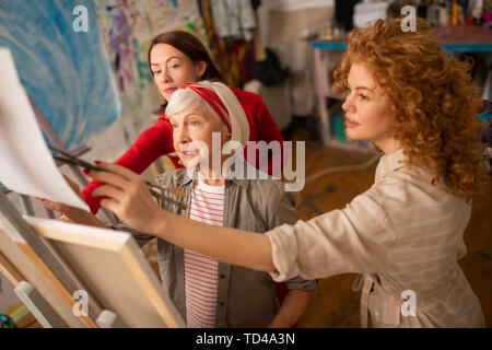 Studenten beitreten. Curly und Dunkelhaarige sich ihre Kunst Lehrer Gemälde auf Leinwand Stockfoto