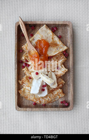 Hausgemachte Pfannkuchen mit Aprikosen Konfitüre, frischem Brie Käse und Rote Johannisbeere auf Holzplatte mit Löffel aus Holz. Ansicht von oben. Stockfoto