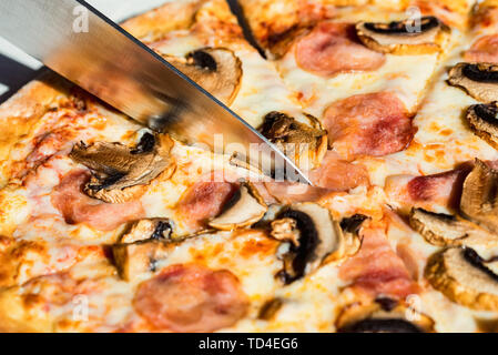 Close up Messer schneiden Pizza mit Salami, Pilzen und Käse aus der Nähe Stockfoto
