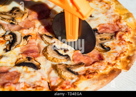 Close up Messer schneiden Pizza mit Salami, Pilzen und Käse aus der Nähe Stockfoto