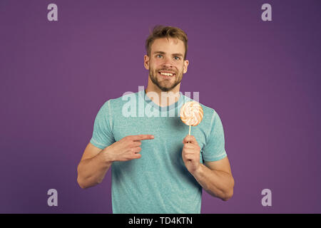 Zucker schädlich für die Gesundheit. Kerl halten Lollipop candy violett unterlegt. Mann schöner macho Essen großen bunten süßen Lutscher. Geschmack der Kindheit. Man bärtige Erwachsene mag Lollipop. Sweet Tooth Konzept. Stockfoto