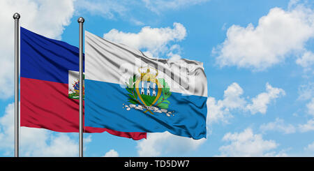 Haiti und San Marino Fahne im Wind gegen Weiße bewölkt blauer Himmel zusammen. Diplomatie Konzept, internationale Beziehungen. Stockfoto