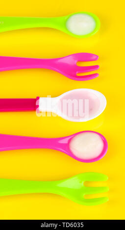 Farbe Löffel und Gabeln für Babynahrung auf gelbem Hintergrund Stockfoto