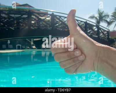 Foto einer Hand tun die OK-Zeichen, und hinter einem Pool mit einer Brücke von einem niedrigen Winkel genommen. Stockfoto