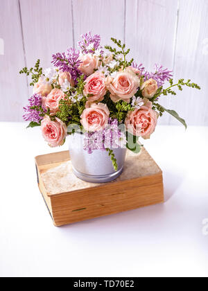 Blumenstrauß aus Rosen und Flieder auf ein altes Buch vor dem Hintergrund der weißen Holzbohlen Stockfoto